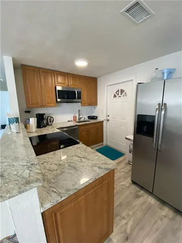 Kitchen featuring appliances with stainless steel finishes, brown cabinetry, light wood-style flooring, and light stone counters