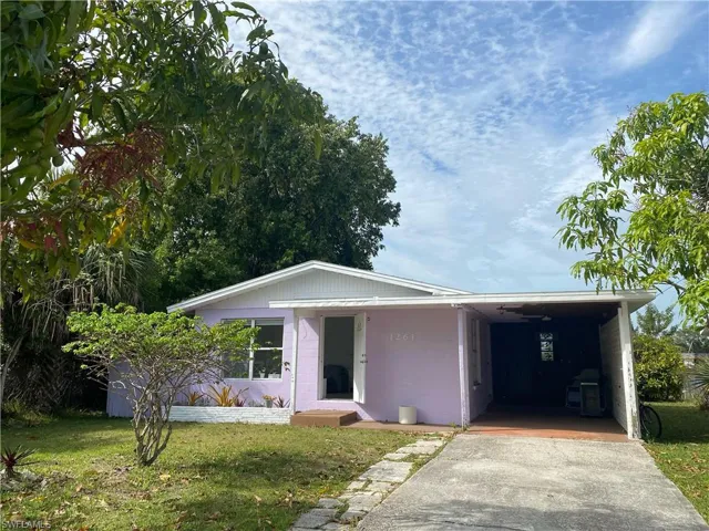 View of front facade featuring a front lawn, concrete block siding, a carport, and driveway