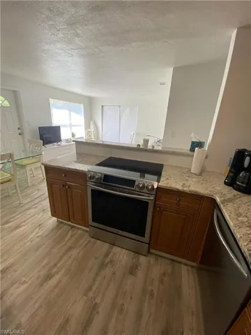 Kitchen featuring brown cabinets, appliances with stainless steel finishes, light stone countertops, light wood-type flooring, and a textured ceiling