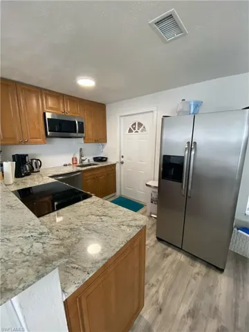 Kitchen with stainless steel appliances, brown cabinetry, light wood-type flooring, light stone counters, and a textured ceiling