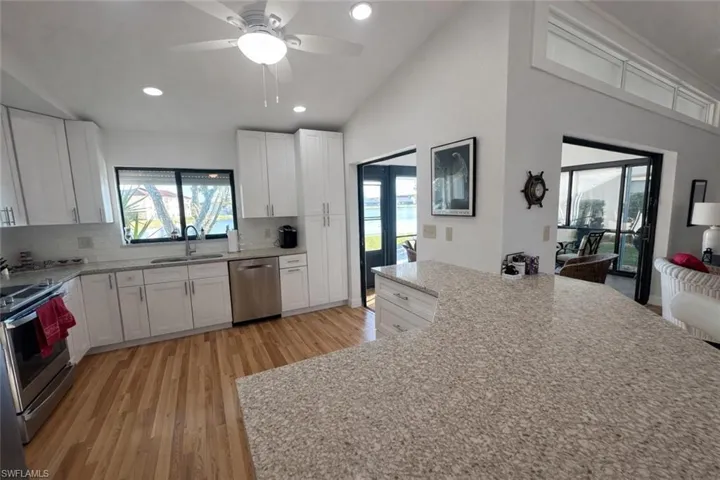 Kitchen with white cabinetry, light stone counters, backsplash, light wood-type flooring, and stainless steel appliances