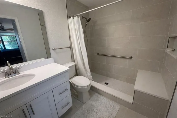 Bathroom featuring vanity, a tile shower, a textured wall, and light tile patterned floors