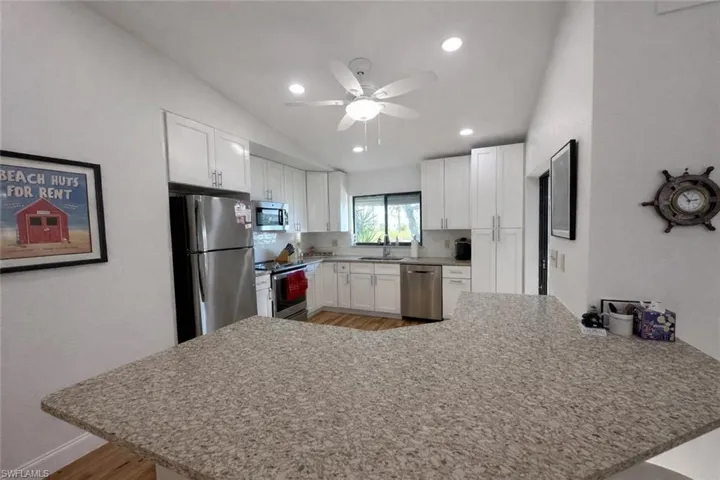 Kitchen featuring a peninsula, stainless steel appliances, white cabinetry, light stone counters, and lofted ceiling