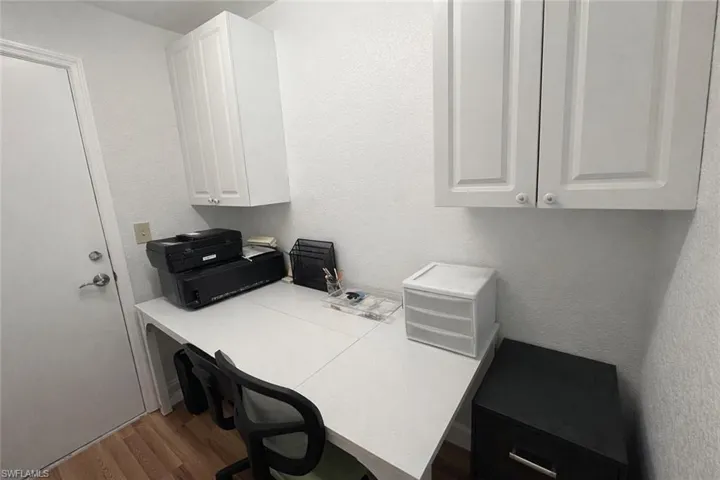 Home office with a textured wall, wood finished floors, and built in desk