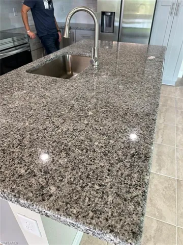 Kitchen view of stainless steel fridge, light stone counters, stove, and a kitchen island with sink