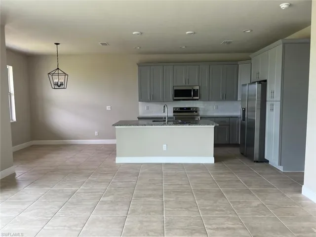 Kitchen featuring stainless steel appliances, decorative backsplash, light stone countertops, a center island with sink, and light tile patterned floors