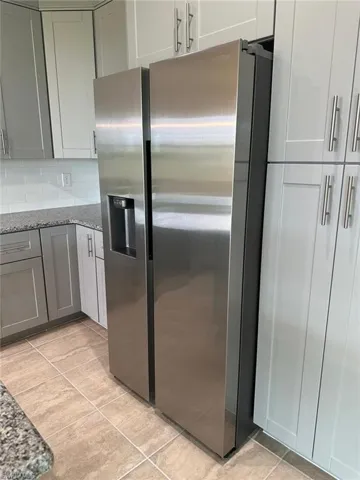 Kitchen featuring stainless steel fridge with ice dispenser, dark stone counters, gray cabinets, decorative backsplash, and light tile patterned flooring