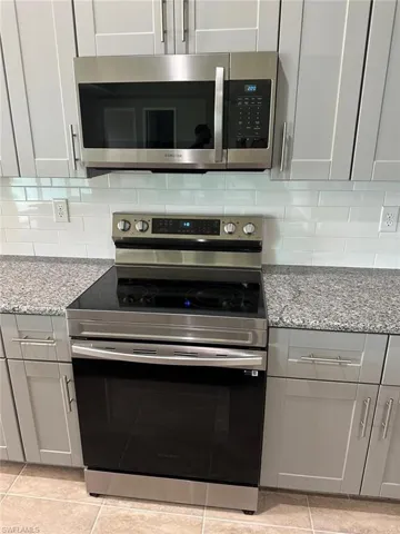 Kitchen with stainless steel appliances, gray cabinetry, light stone counters, and light tile patterned floors
