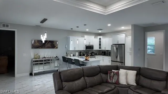 Living room featuring light marble finish flooring, ornamental molding, recessed lighting, and a raised ceiling
