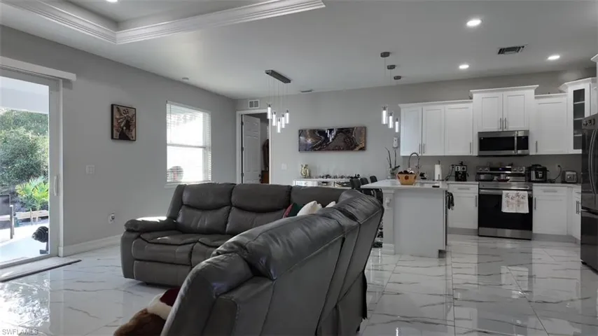 Living area featuring recessed lighting, light marble finish flooring, ornamental molding, and a tray ceiling