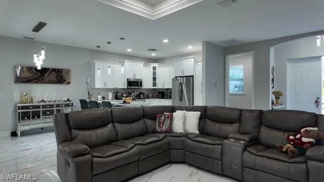 Living room with light marble finish floors, recessed lighting, crown molding, arched walkways, and a tray ceiling