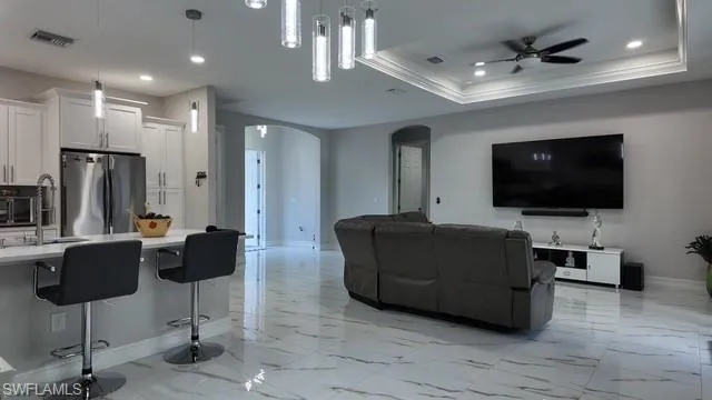 Living area with arched walkways, ceiling fan, recessed lighting, light marble finish floors, and a tray ceiling