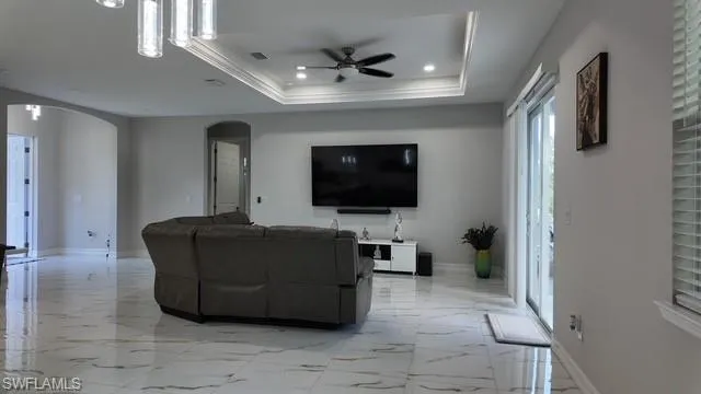 Living area featuring ceiling fan, light marble finish flooring, arched walkways, recessed lighting, and a tray ceiling