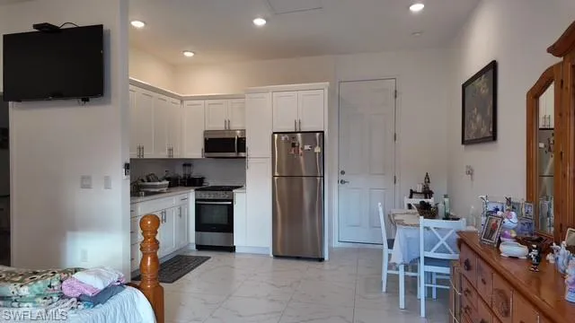 Kitchen with appliances with stainless steel finishes, light marble finish floors, white cabinets, tasteful backsplash, and recessed lighting