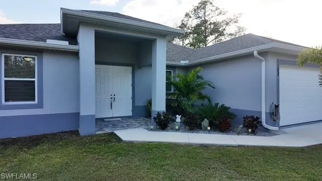 Doorway to property featuring a garage, stucco siding, a lawn, and roof with shingles