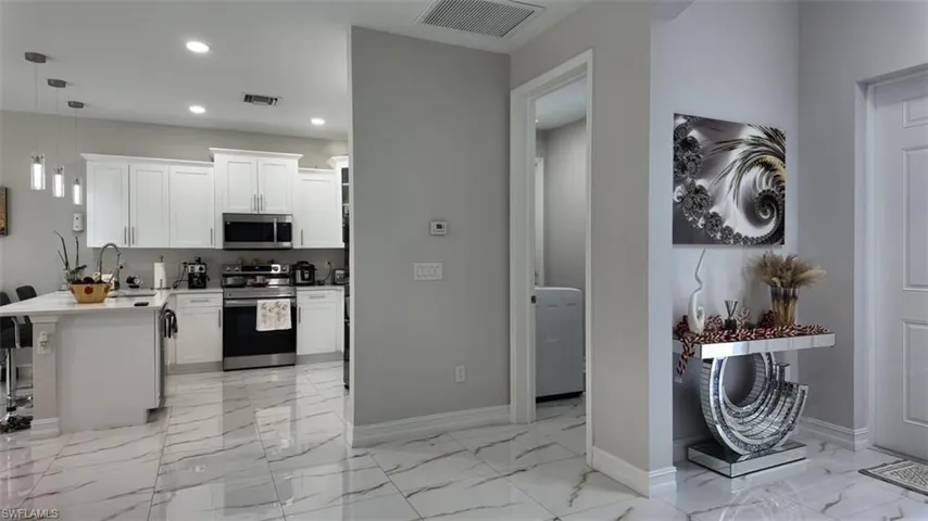 Kitchen with appliances with stainless steel finishes, hanging light fixtures, white cabinetry, a peninsula, and light marble finish floors