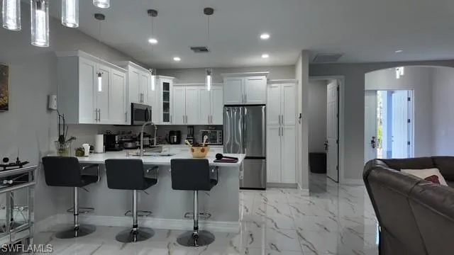 Kitchen featuring glass insert cabinets, appliances with stainless steel finishes, a peninsula, decorative light fixtures, and white cabinetry