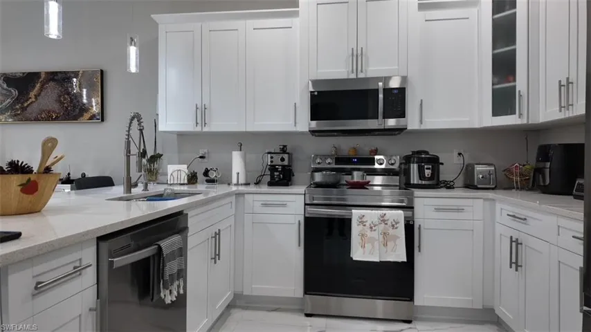 Kitchen with appliances with stainless steel finishes, light stone counters, white cabinetry, and light marble finish floors