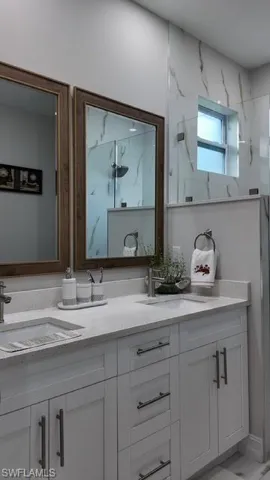 Bathroom featuring double vanity, a marble finish shower, and light marble finish floors