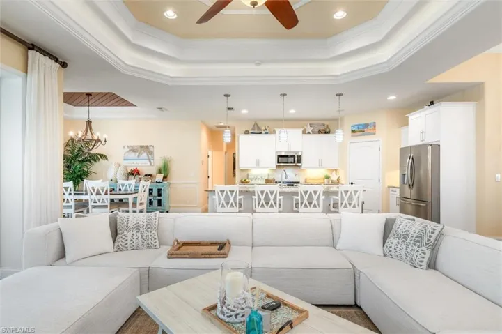 Living room with a raised ceiling, ornamental molding, ceiling fan with notable chandelier, and sink