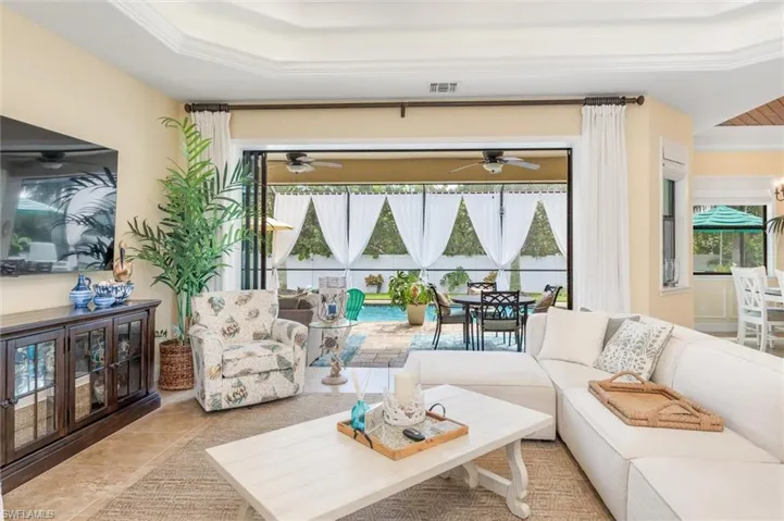 Living room featuring a tray ceiling, light tile patterned floors, crown molding, and ceiling fan