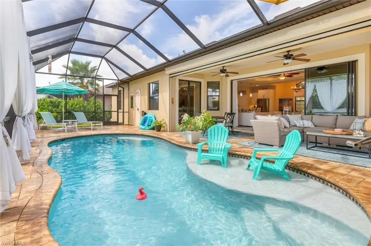 View of pool featuring glass enclosure, ceiling fan, an outdoor hangout area, and a patio