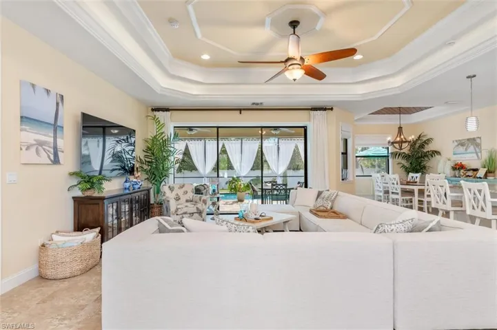 Living room with crown molding, ceiling fan with notable chandelier, and a tray ceiling