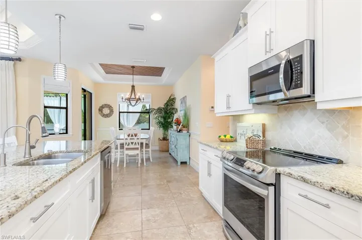 Kitchen with a raised ceiling, pendant lighting, a notable chandelier, appliances with stainless steel finishes, and sink