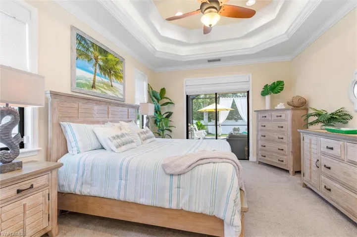Carpeted bedroom with a tray ceiling, ornamental molding, access to exterior, and ceiling fan