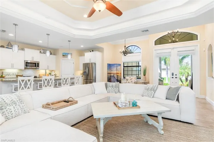Living room with ceiling fan with notable chandelier, a raised ceiling, crown molding, and french doors