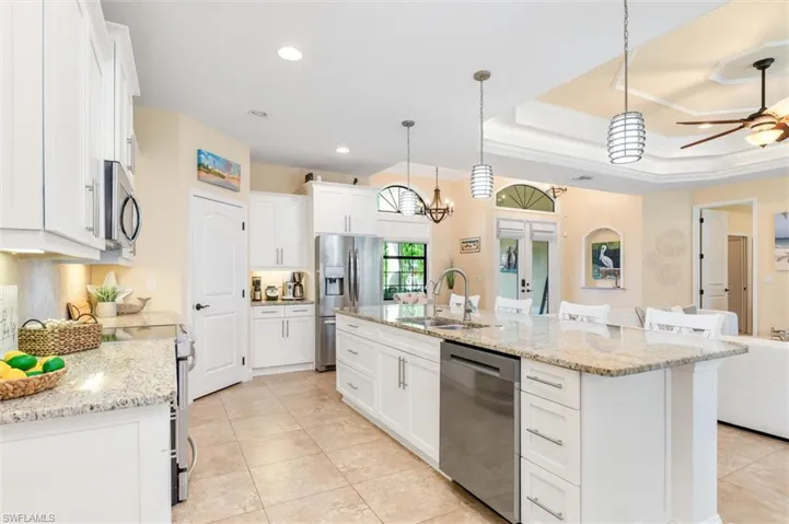 Kitchen with decorative light fixtures, stainless steel appliances, sink, a tray ceiling, and a center island with sink