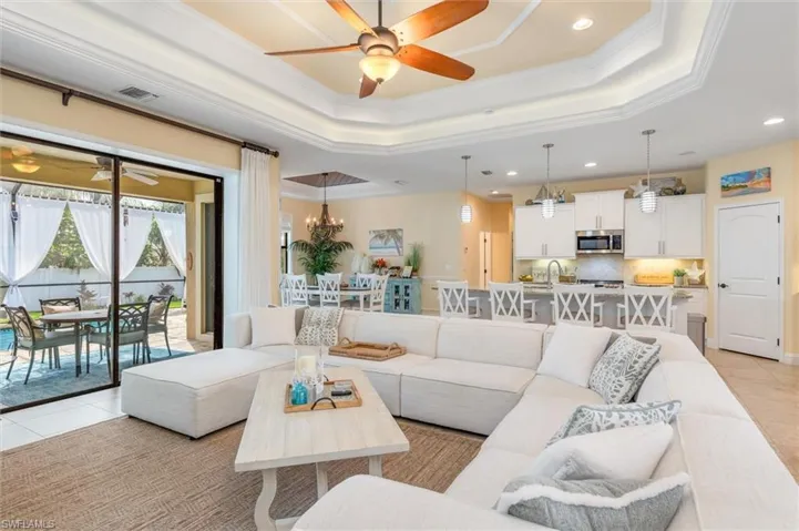 Tiled living room featuring ceiling fan with notable chandelier, crown molding, a tray ceiling, and sink