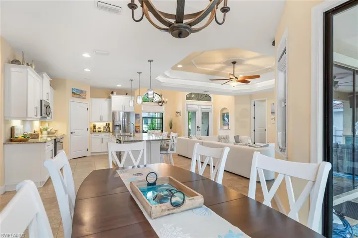 Dining area featuring light tile patterned floors, a raised ceiling, sink, and ceiling fan with notable chandelier