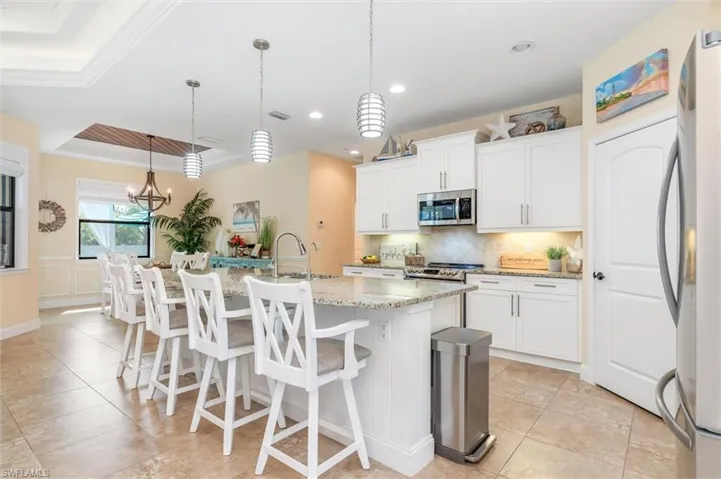 Kitchen featuring white cabinetry, an island with sink, light stone counters, and stainless steel appliances