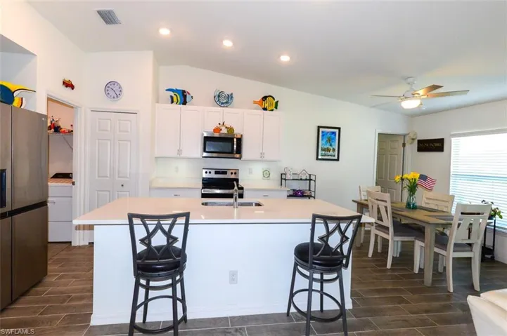 Kitchen featuring wood tiled floors, stainless steel appliances, white cabinetry, a kitchen island with sink, and a kitchen breakfast bar
