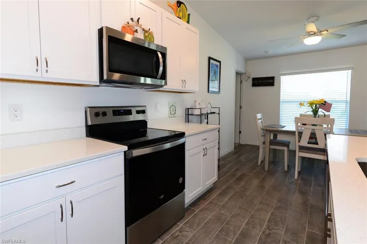 Kitchen with stainless steel appliances, white cabinetry, wood tiled floors, a ceiling fan, and light stone countertops
