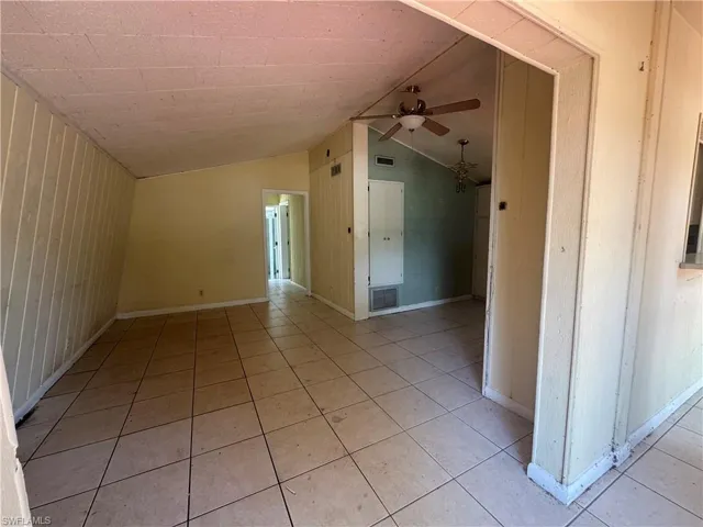 Spare room featuring a ceiling fan, lofted ceiling, wooden walls, and light tile patterned floors