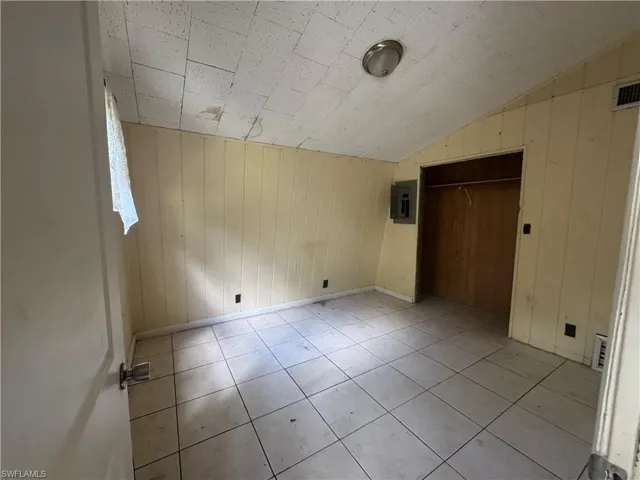Unfurnished bedroom featuring electric panel, a closet, wood walls, light tile patterned flooring, and lofted ceiling