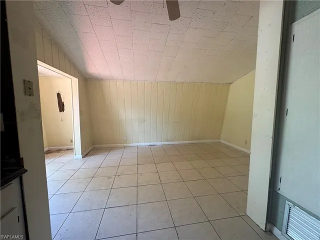Bonus room with wooden walls, ceiling fan, and light tile patterned floors