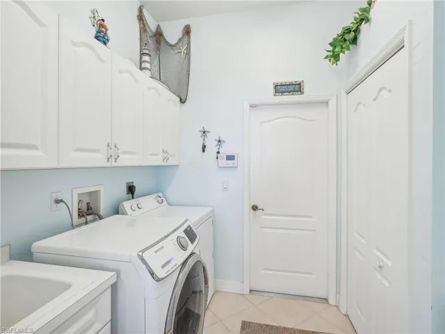 Laundry area with cabinets, light tile patterned floors, separate washer and dryer, and sink