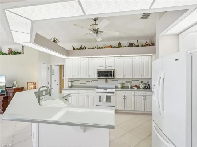 Kitchen featuring white cabinetry, white appliances, sink, and an island with sink