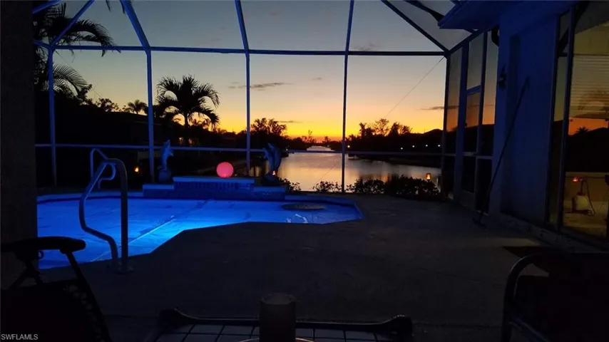 Pool at dusk featuring a lanai, a water view, and a patio