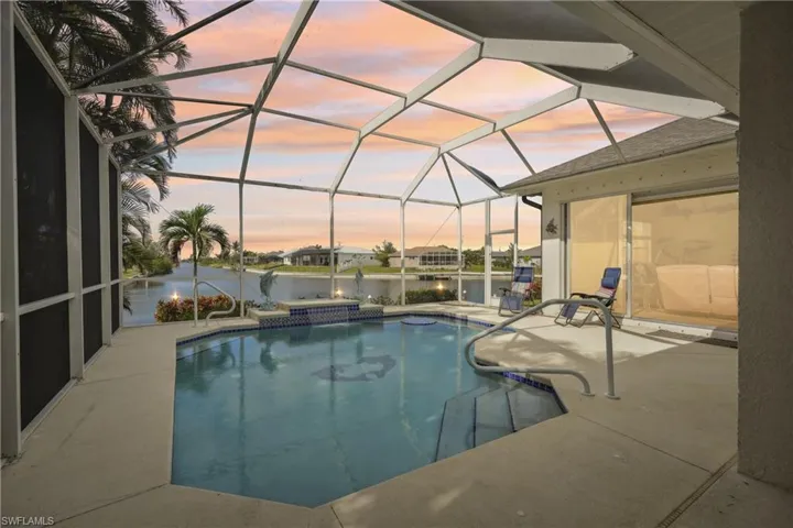 Pool at dusk featuring a lanai, a jacuzzi, a water view, and a patio