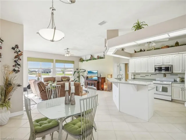 Kitchen with a kitchen island with sink, white stove, hanging light fixtures, ceiling fan, and white cabinetry