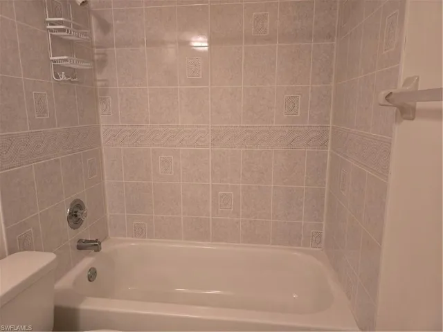 White porcelain bathtub with chrome fixtures and light-colored tiled surround featuring decorative border tiles