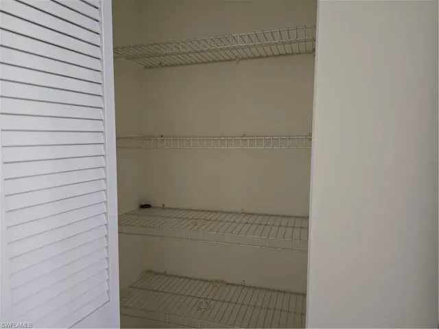 White louvered door opening to a pantry with multiple wire shelves