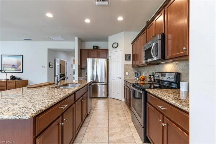 Kitchen with stainless steel appliances, light Granite counters, backsplash and an island with sink