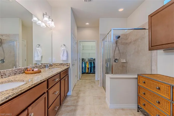 Bathroom with double vanity, a stall shower, a spacious closet, and light tile patterned floors