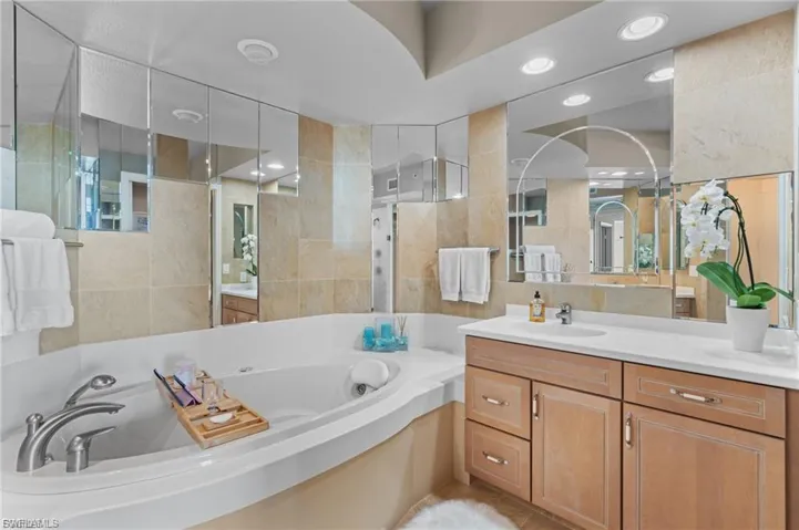 Bathroom featuring a whirlpool tub, vanity, tile walls, recessed lighting, and tiled shower