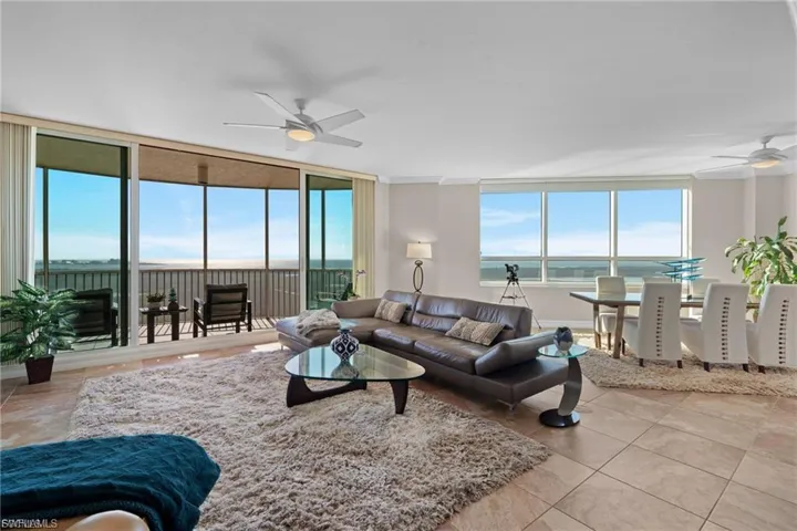 Living room with a ceiling fan, a water view, light tile patterned floors, and a wall of windows